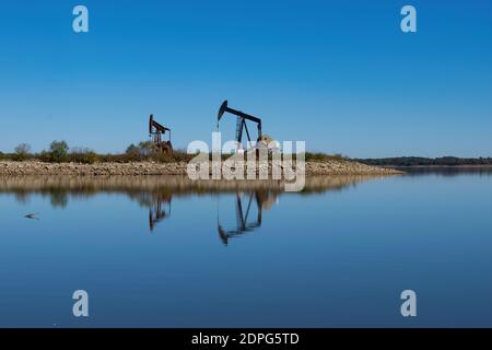 Coppia di martinetti a pompa oleaginosa su una penisola rocciosa che aggirano il lago con i loro riflessi sulla superficie calma e vetrosa dell'acqua. Foto Stock