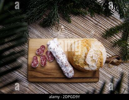 pane e salsiccia si trovano su una tavola di legno, circondata da rami di abete. Foto Stock