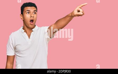 Giovane arabo che indossa abiti casual puntando con un dito sorpreso davanti, bocca aperta stupito espressione, qualcosa sulla parte anteriore Foto Stock
