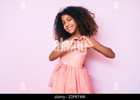 Bambino afroamericano con capelli ricci che indossa la corona della principessa sorridente nell'amore che fa il simbolo del cuore forma con le mani. Concetto romantico. Foto Stock