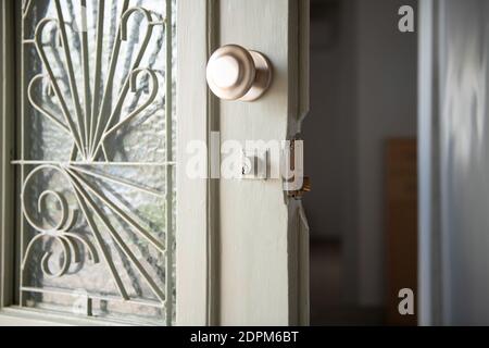 Chiusura di una vecchia casa di porte di legno bianco con vetrate e traliccio di metallo. Porta d'ingresso vintage aperta con maniglia rotonda e serratura della casa rotta Foto Stock