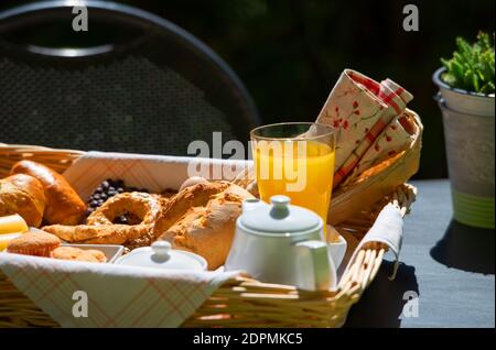 Primo piano della colazione continentale con succo d'arancia, tè e croissant freschi sulla superficie del tavolo sullo sfondo del giardino estivo Foto Stock