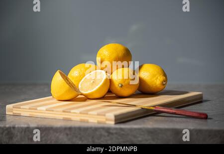 Limoni gialli freschi accatastati sulla superficie del tavolo in pietra di sfondo grigio della cucina in marmo. Mezzo taglio di agrumi a coltello su tavola di legno Foto Stock