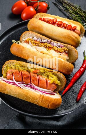Hot dog completamente carico con condimenti assortiti su un vassoio deliziosi hot-dog con salumi di maiale e manzo. Sfondo nero. Vista dall'alto. Foto Stock