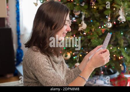 Donna di età universitaria che guarda la cartolina di natale dall'albero di natale Foto Stock