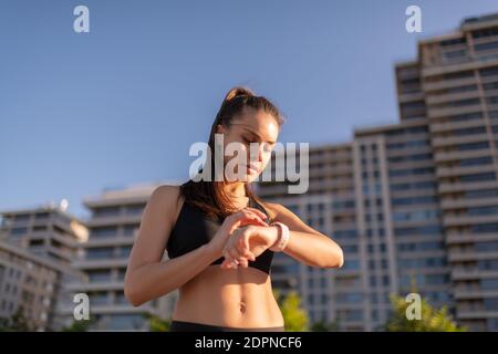 Da sotto runner femminile nella navigazione top del raccolto in intelligente guarda durante l'allenamento su sfondo urbano sfocato Foto Stock