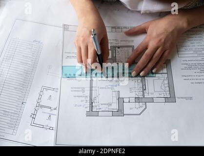 Da sopra designer irriconoscibile utilizzando righello e penna per disegnare linea sulla bozza di costruzione durante i lavori sul progetto in ufficio Foto Stock