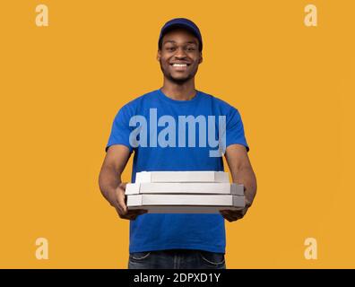 Uomo di consegna nero che tiene le scatole della pizza, dandogli alla macchina fotografica Foto Stock