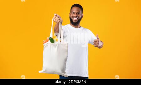 African Man Holding Eco Bag gesturing come, sfondo giallo Foto Stock