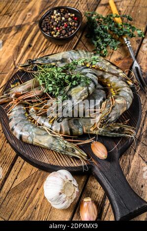 Gamberi neri grezzi di tigre su un tagliere con erbe. Sfondo di legno. Vista dall'alto. Foto Stock