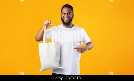 Borsa Eco Smiling Black Guy Holding in piedi su sfondo giallo Foto Stock
