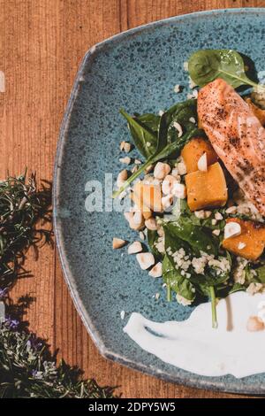 Piatto tipico di pesce fresco, gustoso salmone alla griglia con zucche alla griglia intorno e salsa di yogurt su un tavolo di legno fantasia. Piatti della cucina mediterranea con un Foto Stock