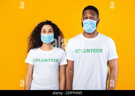 Due volontari che indossano maschere facciali in posa in piedi su sfondo giallo Foto Stock