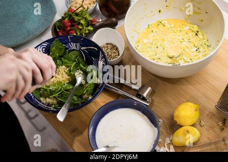 Primo piano di mani di donna che guarniscono un'insalata vegetariana fresca con cous cous. Donna che cucina in cucina a casa preparando cibo sano. Mediterraneo Foto Stock