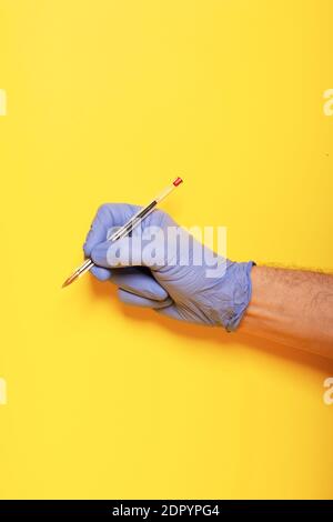 Gesti delle mani. Mano umana in guanto di lattice scrive con la penna a sfera rossa isolata su sfondo giallo con spazio per la copia Foto Stock