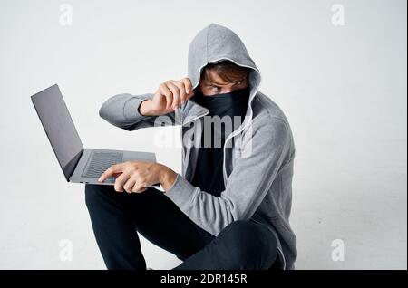 uomo in felpa grigia con computer portatile nascosto maschera hacking Foto Stock