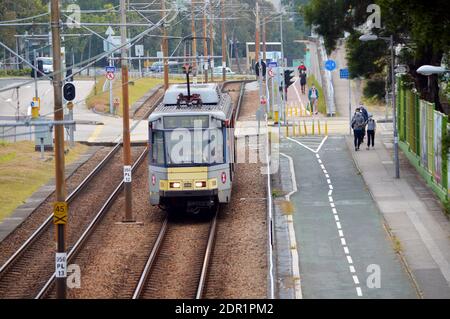 Treno leggero che si avvicina alla fermata Tsing Wun a Tuen Mun, Hong Kong con pista ciclabile e marciapiede Foto Stock