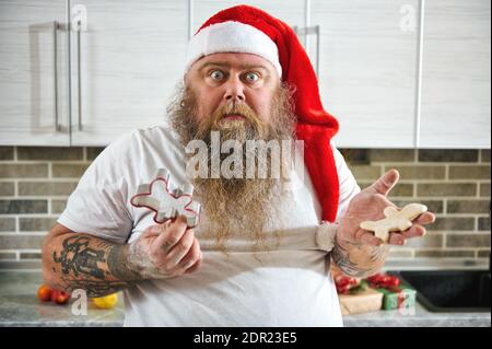 Un uomo sorpreso che indossa come Babbo Natale tenendo un pezzo a forma di persona di pasta su una mano e una taglierina metallica a forma di uomo dall'altro Foto Stock