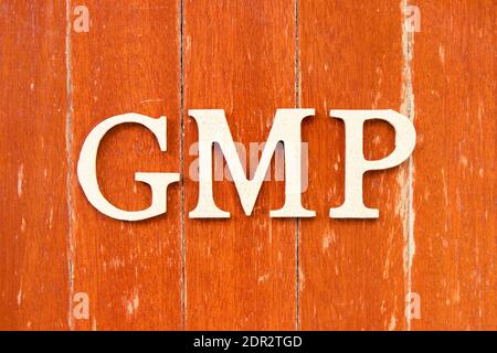 Lettera alfabetica in parola GMP (abbreviazione di buona pratica di fabbricazione) su vecchio sfondo di legno di colore rosso Foto Stock