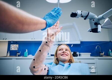Supporto emozionale in ufficio dentista. Dentista che dà high-five alla ragazza nella chirurgia dentale moderna. Foto Stock