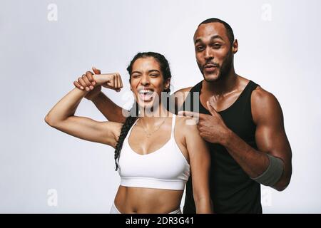 Coppia in abbigliamento fitness in piedi insieme godendo dopo l'allenamento. Donna sorridente che mostra bicipite in piedi con il suo amico maschio. Foto Stock