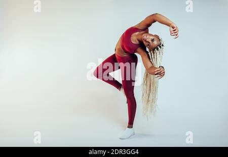 Atleta femminile con lunghi capelli intrecciati che si allenano su sfondo bianco. Adatta donna facendo esercizi di allungamento laterale. Foto Stock