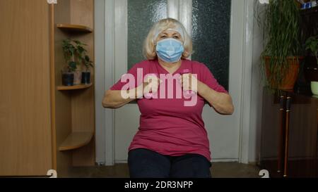 Anziana donna caucasica anziana in abbigliamento sportivo in soggiorno, facendo pesi manubri che si esercitano a casa. Anziano attivo che fa l'allenamento, l'allenamento, il fitness, l'attività sportiva durante il coronavirus Foto Stock