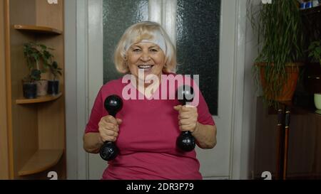 Nonna matura anziana che parla e fa il peso che solleva dumbbell che si esercita a casa. Pensionato attivo che fa allenamento, attività sportiva fitness. Vlog, blog, corso online a distanza Foto Stock