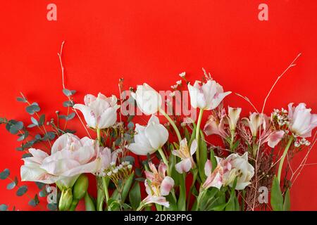 Tulipani bianchi alstroemeria rami e foglia verde su sfondo rosso con spazio copia. Carta da parati dolce e bella per il design dello sfondo di Valentine Foto Stock