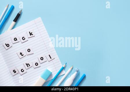 Testo Torna a scuola scritto da lettere stampate su bianco fogli di carta su notebook con cartoleria blu su sfondo blu con uno spazio per la copia Foto Stock