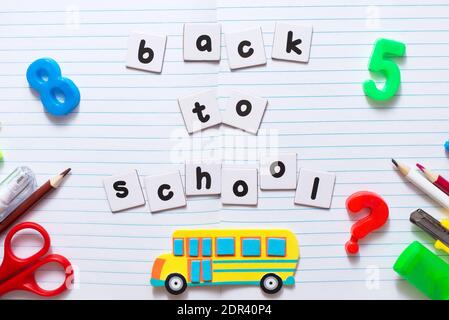 Testo di ritorno a scuola su foglio di notebook con colorato cartoleria scolastica e autobus giocattolo giallo Foto Stock