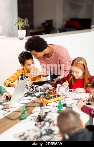 Smily African American insegnante di scienza femminile con gruppo di bambini programmazione di giocattoli e robot elettrici in classe robotica Foto Stock