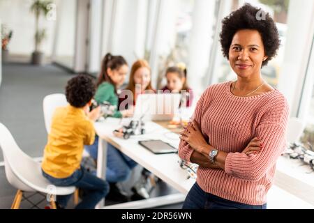 Smily African American insegnante di scienza femminile con gruppo di bambini programmazione di giocattoli e robot elettrici in classe robotica Foto Stock