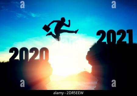 2021, calendario. Silhouette di un uomo d'affari che salta su una scogliera, da una scogliera all'altra. Sullo sfondo, il cielo e la luce solare. La conce Foto Stock