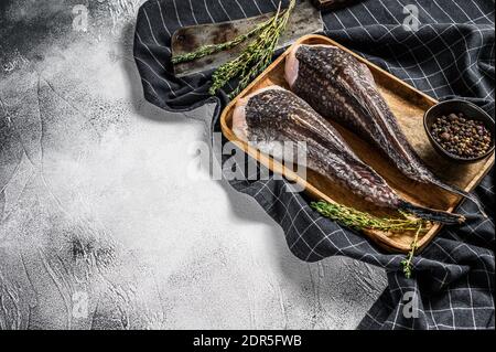 Pesce monaco fresco senza testa su un vassoio di legno con una scissione. Sfondo grigio. Vista dall'alto. Spazio di copia. Foto Stock