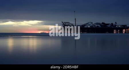 Vista panoramica del mare calmo con la bassa marea con Brighton Palace Pier dopo il tramonto Foto Stock