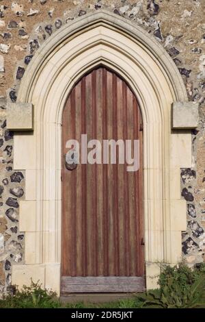 Porta d'epoca in legno ad arco incastonata in un'architettura murale in pietra, St Margaret's Church, Rottingdean, East Sussex, Inghilterra, in formato verticale Foto Stock