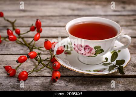 Una tazza di tè alla rosa con fianchi di rose freschi su un tavolo di legno. Foto Stock