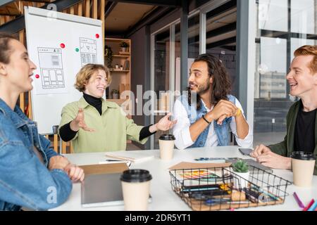 Giovane gioiosa donna d'affari in casualwear guardando uno di maschio colleghi con un sorriso togoloso durante la discussione di idee per il progetto Foto Stock