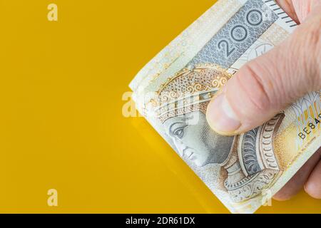Un pacchetto di denaro polacco, duecento banconote zloty, tenuto in mano. Sfondo giallo con posizione per il testo Foto Stock