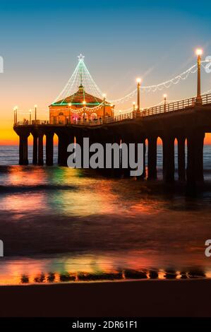 Scatto verticale del molo di Manhattan Beach fotografato illuminato dopo il tramonto durante il periodo natalizio a Manhattan Beach, California. Foto Stock