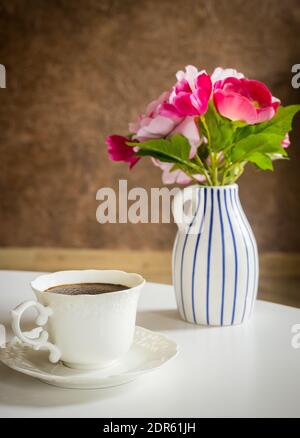 Una tazza di caffè nero sul tavolo dietro di esso una pentola elegante con un bouquet di fiori Foto Stock