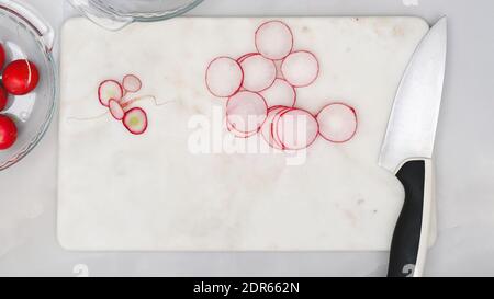 Ravanello fresco affettato primo piano su tagliere in marmo su sfondo grigio chiaro. Preparazione insalata vegetale, ricetta Foto Stock