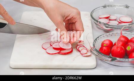 Ravanello fresco affettato primo piano su tagliere in marmo su sfondo grigio chiaro. Preparazione insalata vegetale, ricetta Foto Stock