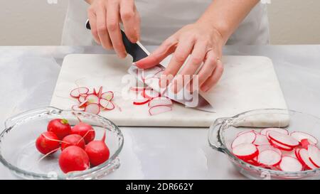 Ravanello fresco affettato primo piano su tagliere in marmo su sfondo grigio chiaro. Preparazione insalata vegetale, ricetta Foto Stock