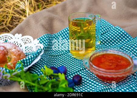 Picnic in natura in autunno. Tè verde con menta in una tazza di vetro, una ciotola con confetture di frutti di bosco e dolci freschi. Riposo e relax. Foto Stock