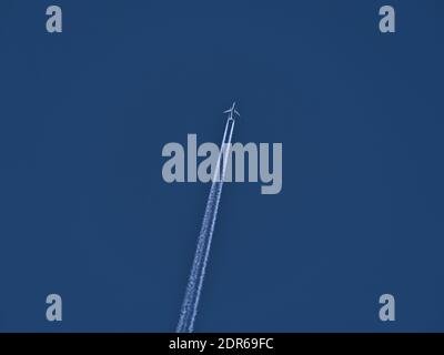 Vista ad angolo basso di un alto velivolo bimotore con percorso di condensazione di colore bianco in cielo blu chiaro. Foto Stock