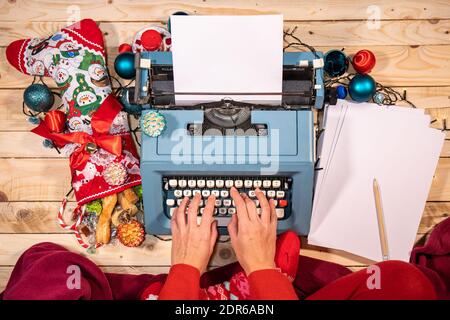 Atmosfera natalizia con una macchina da scrivere vintage, calze piene di dolci, una coperta rossa e un mucchio di fogli bianchi. Foto Stock