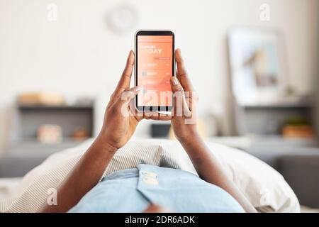 POV della giovane afroamericana che tiene lo smartphone a letto mentre ascolta la musica al mattino, spazio di copia Foto Stock