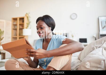 Ritratto di donna afroamericana sorridente seduta a letto al mattino e utilizzando tablet digitale con auricolari wireless, spazio di copia Foto Stock